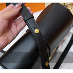 Close-up of a black leather bag with gold buttons held by a hand.