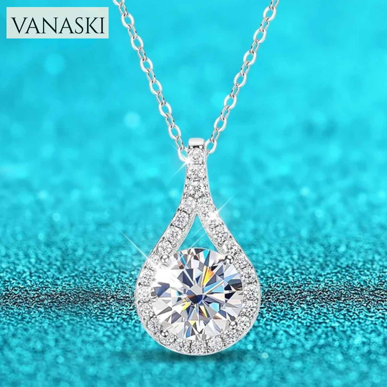 Teardrop-shaped diamond pendant necklace on a blue glittery background with 'VANASKI' branding.